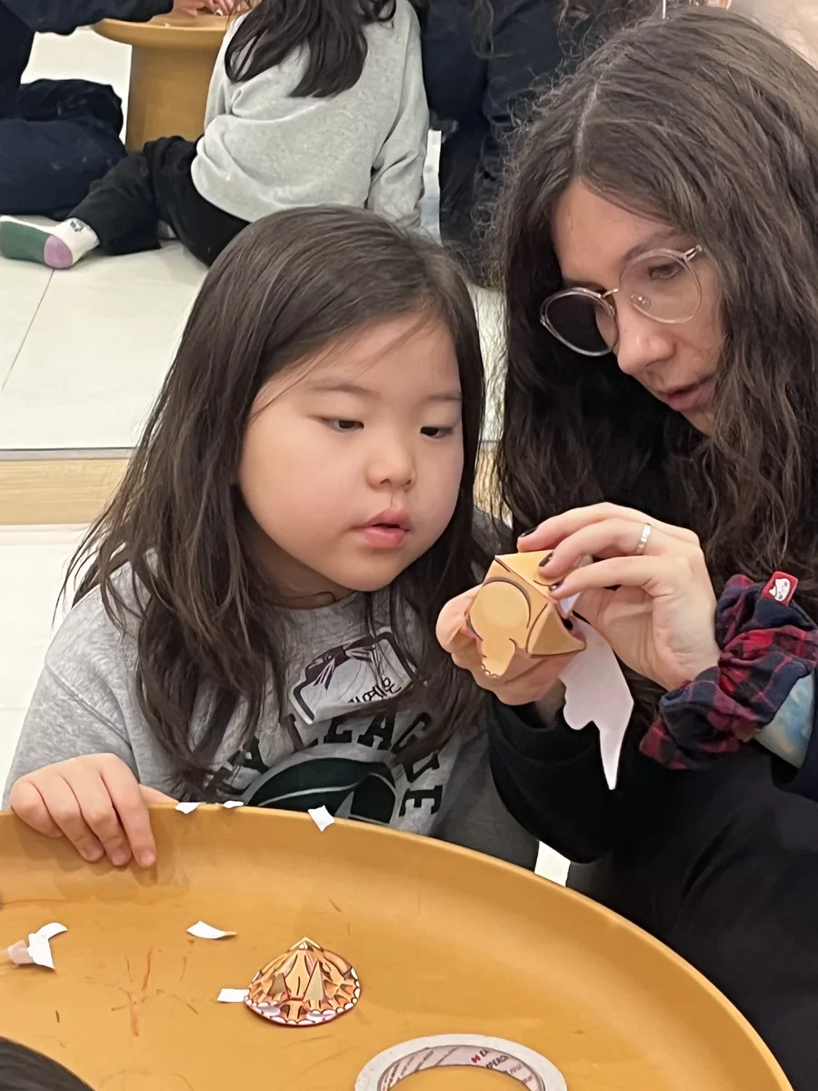 원어민 선생님과 마주 앉아 종이 만들기를 하는 아이